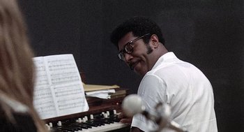 Movie still from “Taking Off” (1971), directed by Milos Forman – A man sitting at a keyboard with a sheet of music on it; Close Up shot, Low angle