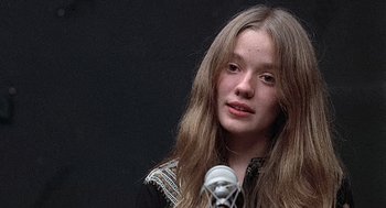 Movie still from “Taking Off” (1971), directed by Milos Forman – A young girl with long brown hair is speaking into a microphone; Close Up shot, Low angle