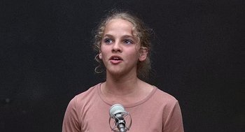 Movie still from “Taking Off” (1971), directed by Milos Forman – A young girl is speaking into a microphone in front of a black background; Close Up shot, Low angle