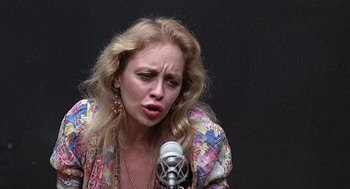 Movie still from “Taking Off” (1971), directed by Milos Forman – A woman with blonde hair is singing into a microphone; Close Up shot, High angle