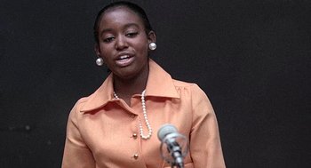 Movie still from “Taking Off” (1971), directed by Milos Forman – A woman in an orange shirt is speaking into a microphone; Close Up shot, Low angle
