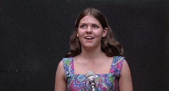 Movie still from “Taking Off” (1971), directed by Milos Forman – A woman with long hair is singing into a microphone; Close Up shot, Low angle