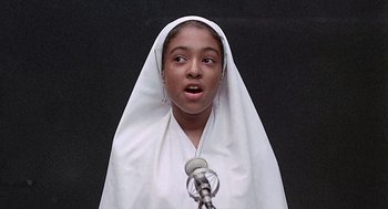 Movie still from “Taking Off” (1971), directed by Milos Forman – A young girl wearing a white robe and a white head covering; Close Up shot, Low angle