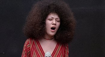 Movie still from “Taking Off” (1971), directed by Milos Forman – A woman with a big afro singing into a microphone; Medium shot, Low angle