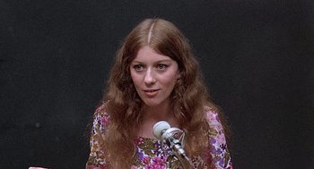 Movie still from “Taking Off” (1971), directed by Milos Forman – A woman with brown hair is speaking into a microphone; Close Up shot, High angle