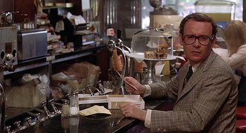 Movie still from “Taking Off” (1971), directed by Milos Forman – A man sitting at a counter in front of a plate of food; Medium shot, Over the shoulder angle
