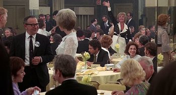 Movie still from “Taking Off” (1971), directed by Milos Forman – A group of people sitting at tables in a banquet hall; Wide shot, Over the shoulder angle