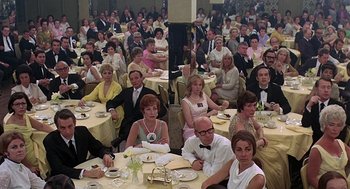 Movie still from “Taking Off” (1971), directed by Milos Forman – A group of people sitting at tables in a room; Wide shot, High angle