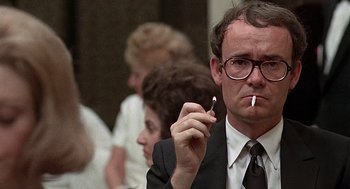 Movie still from “Taking Off” (1971), directed by Milos Forman – A man in a suit and tie smoking a cigarette; Close Up shot, Low angle