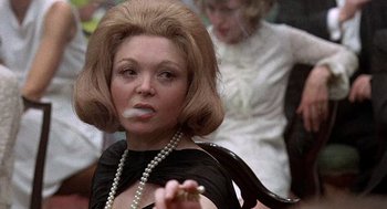 Movie still from “Taking Off” (1971), directed by Milos Forman – A woman smoking a cigarette while wearing a black dress; Close Up shot, Low angle