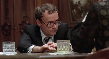 Movie still from “Taking Off” (1971), directed by Milos Forman – A man sitting at a wooden table with a glass of water; Close Up shot, Over the shoulder angle