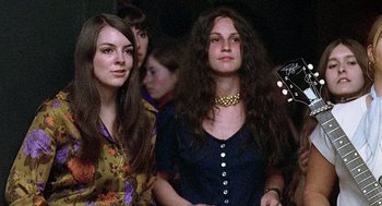 Movie still from “Taking Off” (1971), directed by Milos Forman – Two young women are posing for a picture while holding a guitar; Medium shot, Low angle