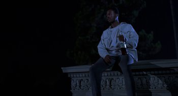 Movie still from “Tales from the Hood” (1995), directed by Rusty Cundieff – A man sitting on a bench holding a bottle of beer; Medium shot, Low angle