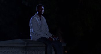 Movie still from “Tales from the Hood” (1995), directed by Rusty Cundieff – A man sitting on top of a stone pillar; Medium shot, Low angle