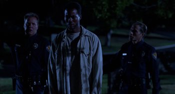 Movie still from “Tales from the Hood” (1995), directed by Rusty Cundieff – A man standing in the dark next to two police officers; Medium shot, Low angle