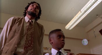 Movie still from “Tales from the Hood” (1995), directed by Rusty Cundieff – A man standing next to a young boy in a room; Medium shot, Low angle