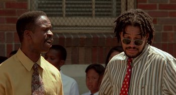Movie still from “Tales from the Hood” (1995), directed by Rusty Cundieff – Two men standing next to each other in front of a group of people; Close Up shot, Low angle
