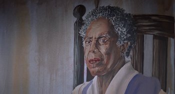 Movie still from “Tales from the Hood” (1995), directed by Rusty Cundieff – An older woman with curly grey hair is painted on the wall; Close Up shot, Low angle