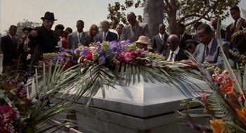 Movie still from “Tales from the Hood” (1995), directed by Rusty Cundieff – A group of people gathered around a white coffin; Wide shot, High angle