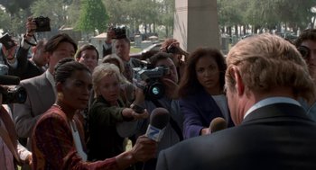 Movie still from “Tales from the Hood” (1995), directed by Rusty Cundieff – A group of people gathered around a man holding a microphone; Medium shot, Over the shoulder angle