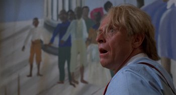 Movie still from “Tales from the Hood” (1995), directed by Rusty Cundieff – An older woman with blonde hair is looking up at a painting; Close Up shot, Low angle