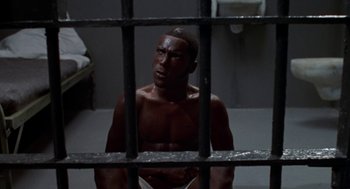 Movie still from “Tales from the Hood” (1995), directed by Rusty Cundieff – A man sitting behind bars in a jail cell; Medium shot, High angle