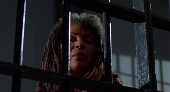 Movie still from “Tales from the Hood” (1995), directed by Rusty Cundieff – A woman with dreadlocks is behind a metal fence; Close Up shot, Low angle