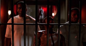 Movie still from “Tales from the Hood” (1995), directed by Rusty Cundieff – A group of men standing next to each other in front of bars; Medium shot, Low angle