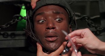 Movie still from “Tales from the Hood” (1995), directed by Rusty Cundieff – A man is getting his face waxed by a person; Close Up shot, High angle
