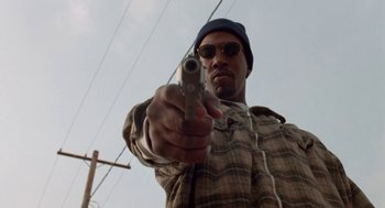 Movie still from “Tales from the Hood” (1995), directed by Rusty Cundieff – A man holding a gun while standing next to power lines; Close Up shot, Low angle