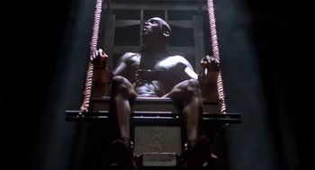 Movie still from “Tales from the Hood” (1995), directed by Rusty Cundieff – A man sitting in a chair with ropes around it; Wide shot, High angle