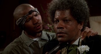 Movie still from “Tales from the Hood” (1995), directed by Rusty Cundieff – Two men one of whom is holding a microphone and the other one is holding a microphone; Close Up shot, Low angle