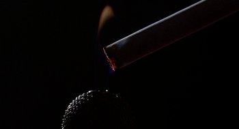 Movie still from “Talk Radio” (1988), directed by Oliver Stone – A lit cigarette on top of a black background; Extreme Close Up shot, Overhead angle