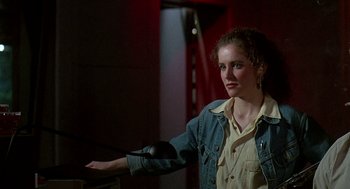 Movie still from “Talk Radio” (1988), directed by Oliver Stone – A woman standing in front of a microphone in a dark room; Medium shot, Low angle