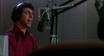 Movie still from “Talk Radio” (1988), directed by Oliver Stone – A man standing in front of a microphone in a room; Close Up shot, Low angle