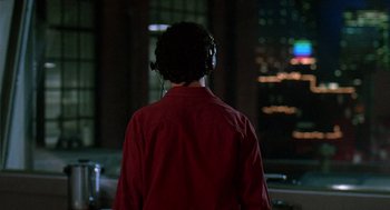 Movie still from “Talk Radio” (1988), directed by Oliver Stone – A person wearing headphones in a room with a city view; Medium shot, Over the shoulder angle