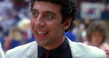 Movie still from “Talk Radio” (1988), directed by Oliver Stone – A person wearing a suit and tie smiling; Close Up shot, Low angle