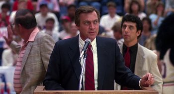 Movie still from “Talk Radio” (1988), directed by Oliver Stone – A man in a suit and tie speaking at a podium; Medium shot, Low angle