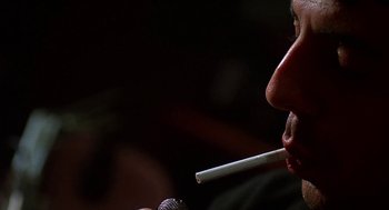 Movie still from “Talk Radio” (1988), directed by Oliver Stone – A man holding a cigarette in his mouth while holding a microphone in front of his face; Extreme Close Up shot, Low angle