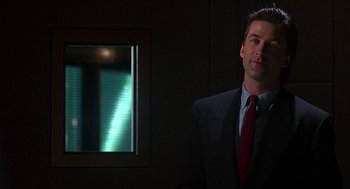 Movie still from “Talk Radio” (1988), directed by Oliver Stone – A man wearing a suit and tie in a dark room; Medium shot, Low angle