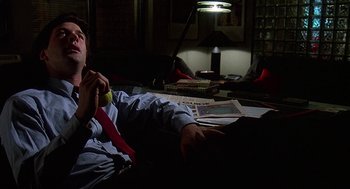 Movie still from “Talk Radio” (1988), directed by Oliver Stone – A man sitting on a couch in a dark room holding an apple; Medium shot, High angle