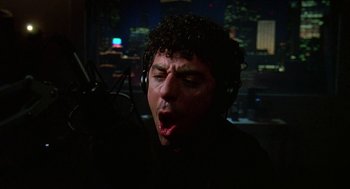 Movie still from “Talk Radio” (1988), directed by Oliver Stone – A man wearing headphones and singing into a microphone; Close Up shot, Low angle