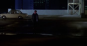 Movie still from “Talk Radio” (1988), directed by Oliver Stone – A man standing in a parking lot at night; Wide shot, Low angle
