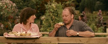 Movie still from “Tamara Drewe” (2010), directed by Stephen Frears – An older man and a younger woman are eating a sandwich; Medium shot, Over the shoulder angle