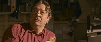 Movie still from “Tamara Drewe” (2010), directed by Stephen Frears – A man in a red shirt is holding a piece of food; Close Up shot, Over the shoulder angle