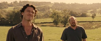Movie still from “Tamara Drewe” (2010), directed by Stephen Frears – Two men standing in a grassy field with trees in the background; Medium shot, Over the shoulder angle