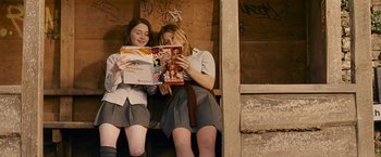 Movie still from “Tamara Drewe” (2010), directed by Stephen Frears – Two young women sitting on a bench reading a magazine; Medium shot, Low angle