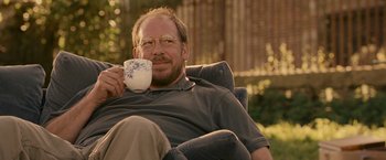 Movie still from “Tamara Drewe” (2010), directed by Stephen Frears – A man sitting in a chair holding a cup; Medium shot, Over the shoulder angle