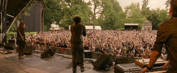 Movie still from “Tamara Drewe” (2010), directed by Stephen Frears – A crowd of people watching a man on a stage; Wide shot, Over the shoulder angle
