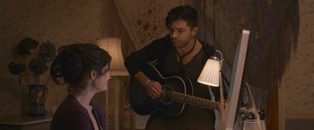 Movie still from “Tamara Drewe” (2010), directed by Stephen Frears – A man playing a guitar while a woman watches; Medium shot, Over the shoulder angle